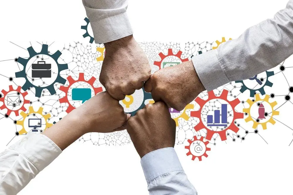 Puños unidos sobre iconos de engranajes con símbolos de comunicación y CRM, representando la capa relacional de un ecosistema SaaS