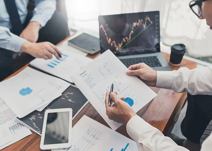 Equipo revisando informes financieros impresos y gráficos en un portátil, representando los fallos del presupuesto tradicional