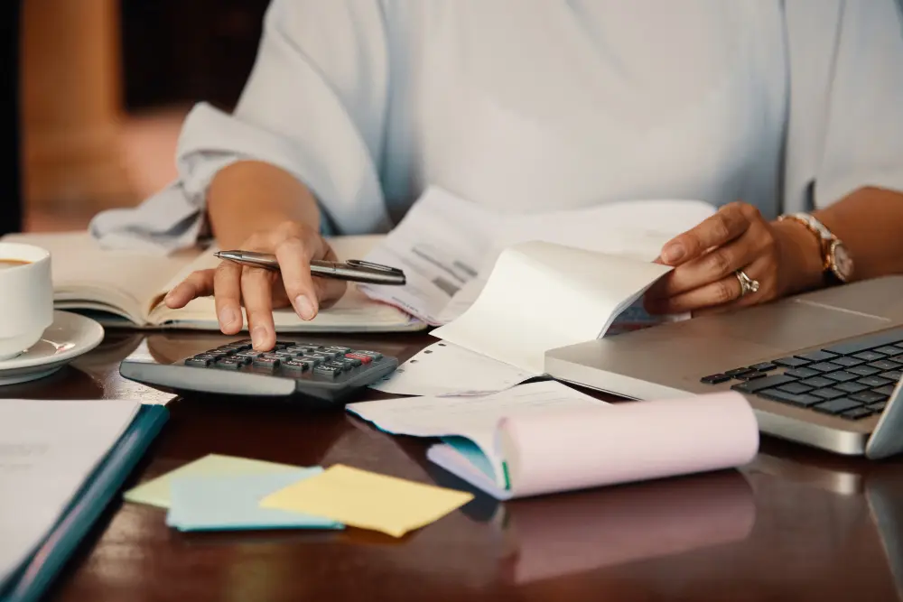 Manos usando una calculadora y revisando recibos junto a un portátil, representando la transición hacia presupuestos invisibles y automatizados