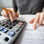 Persona usando una calculadora junto a un documento con cifras financieras, representando la organización de las finanzas personales con herramientas de gestión