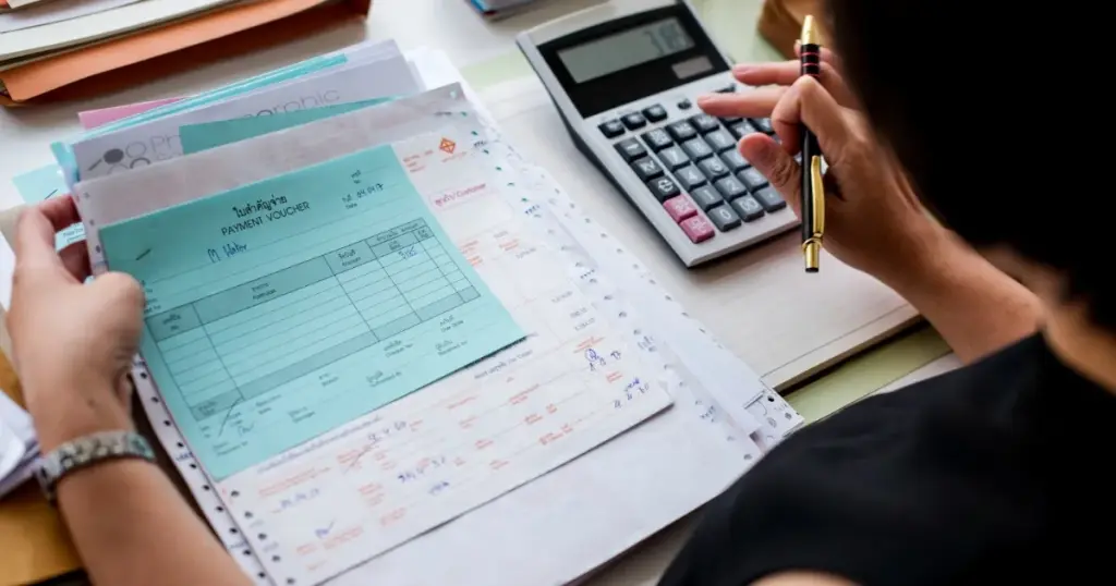 Persona revisando facturas y comprobantes de pago con una calculadora, representando el error de llevar presupuestos demasiado complejos
