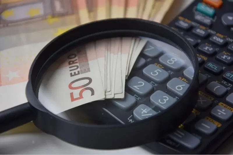 Lupa sobre un billete de 50 euros y una calculadora, representando la priorización y el orden de los gastos financieros