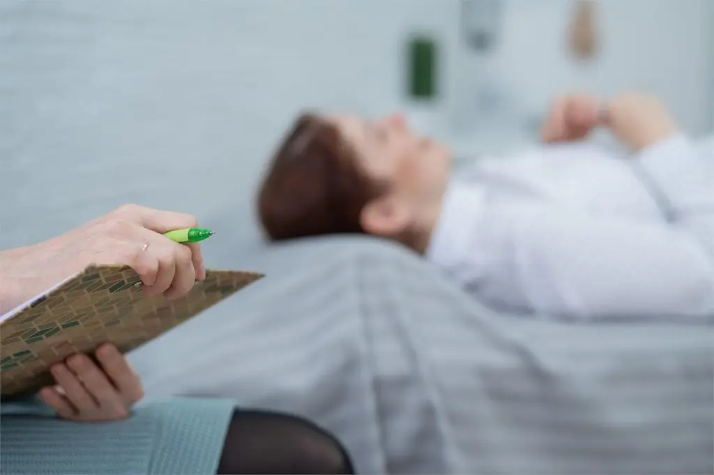 Persona en una consulta de terapia tumbada mientras un profesional toma notas, representando la psicología detrás de la calma financiera
