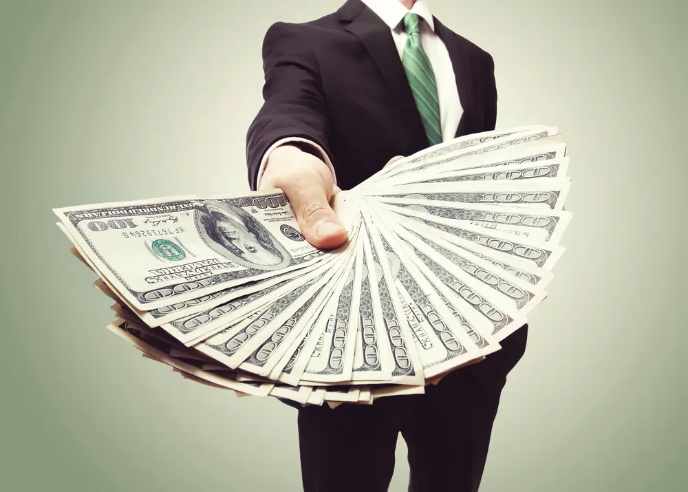 Hombre de traje entregando un fajo de billetes, representando la creación de un sueldo estable a partir de ingresos variables